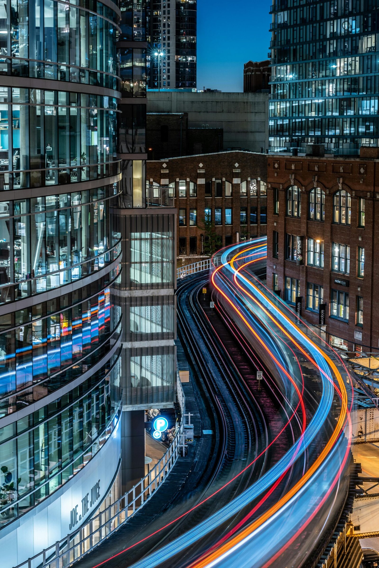 Long exposure of urban train tracks creating vibrant light trails in a modern cityscape at night.